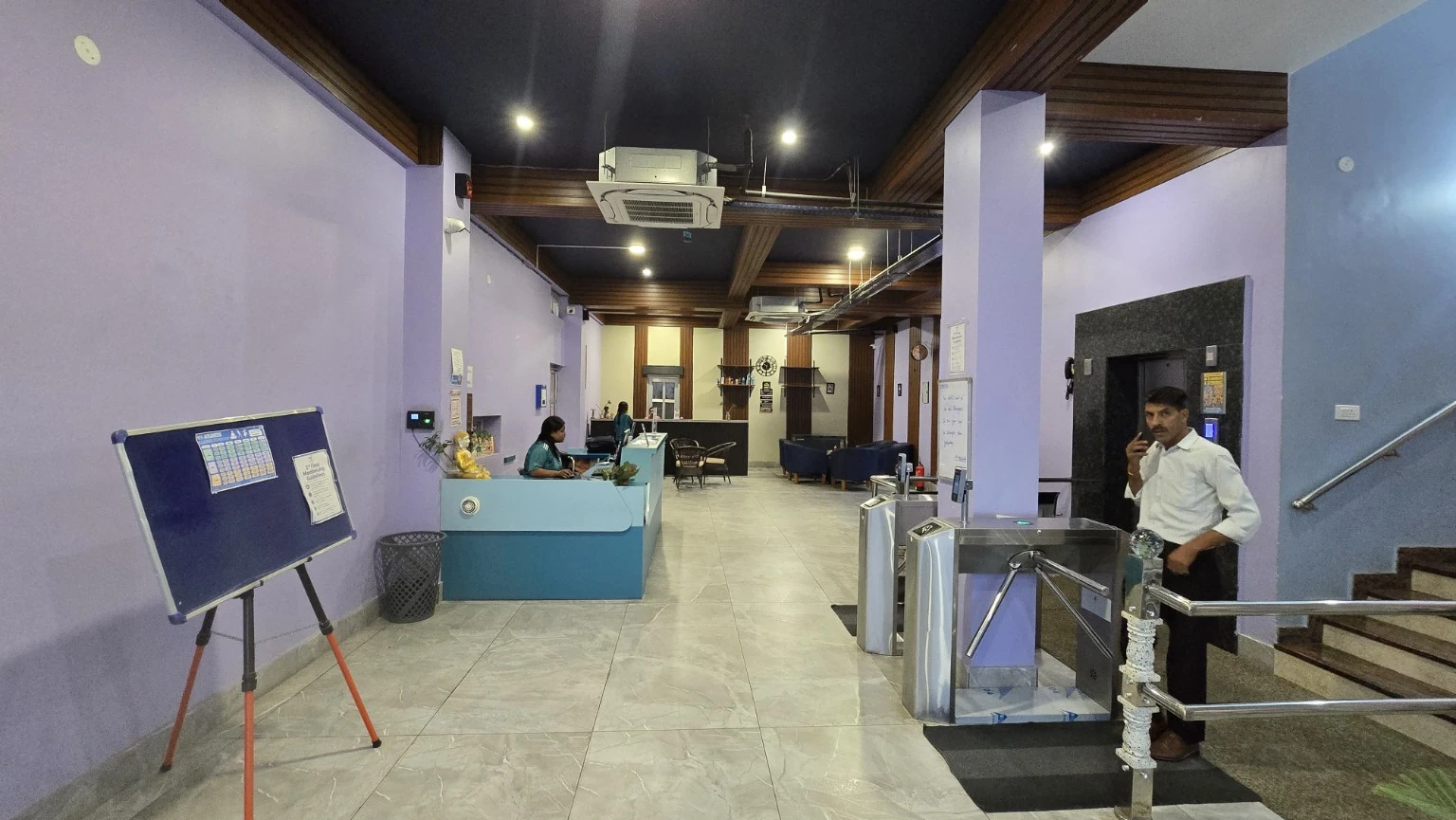 Entrance lobby with turquoise reception desk, access gates, lift, stairs and café at the back