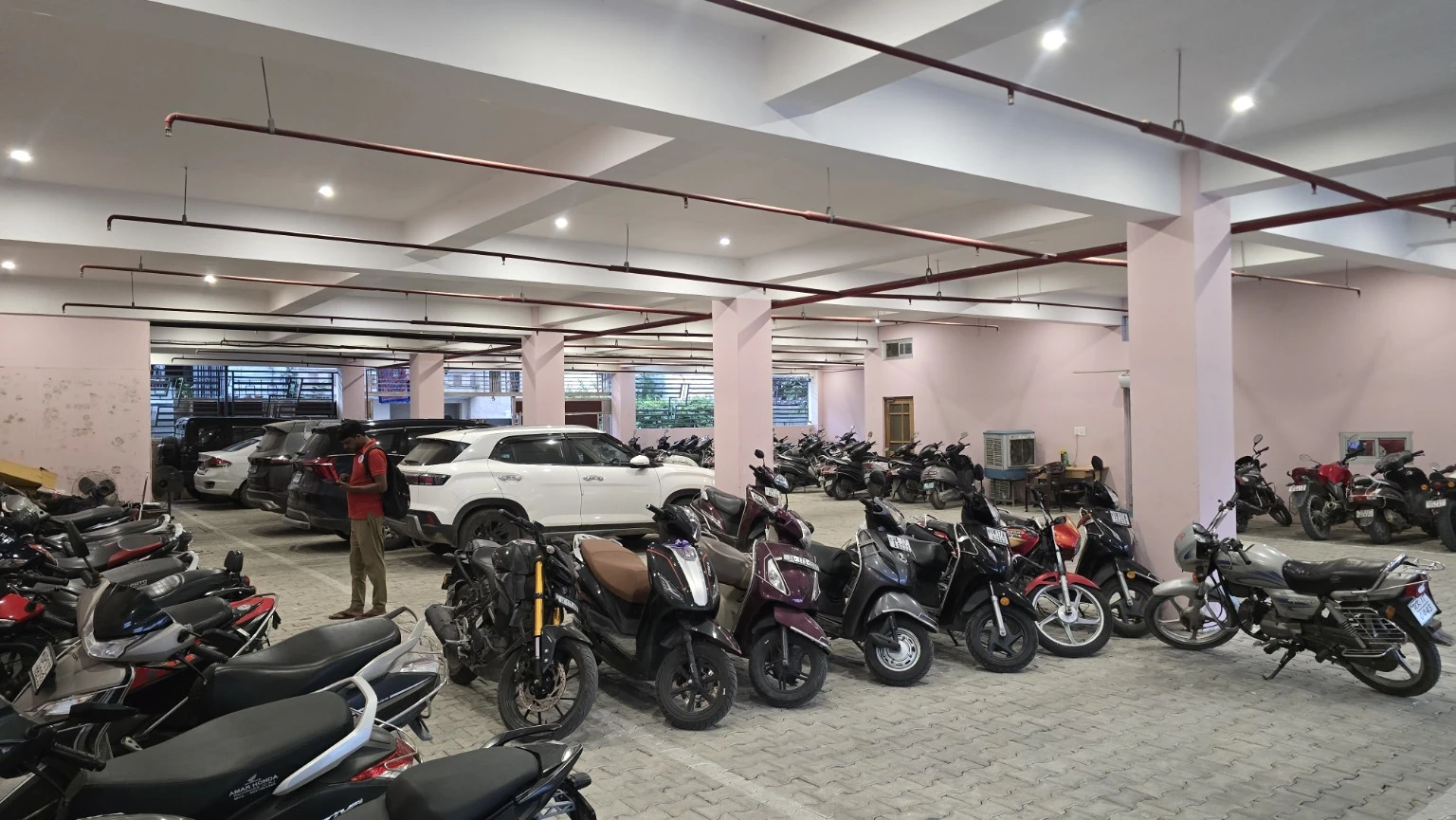 Wide covered parking area with cars, scooters and motorcycles between pale columns