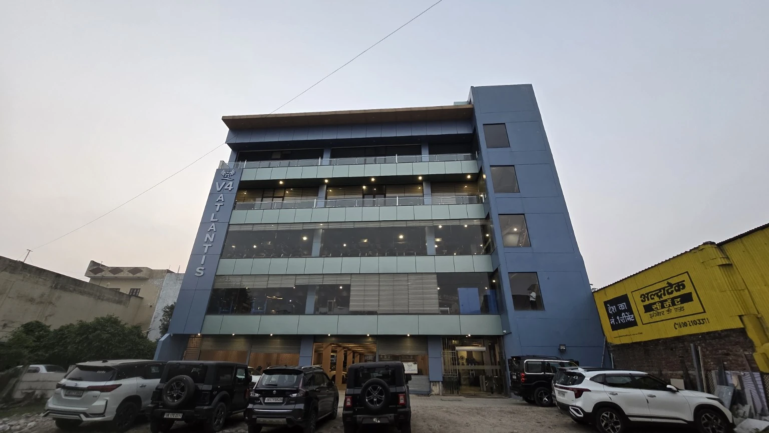 V4 ATLANTIS building at dusk with blue facade, vertical signage and cars outside