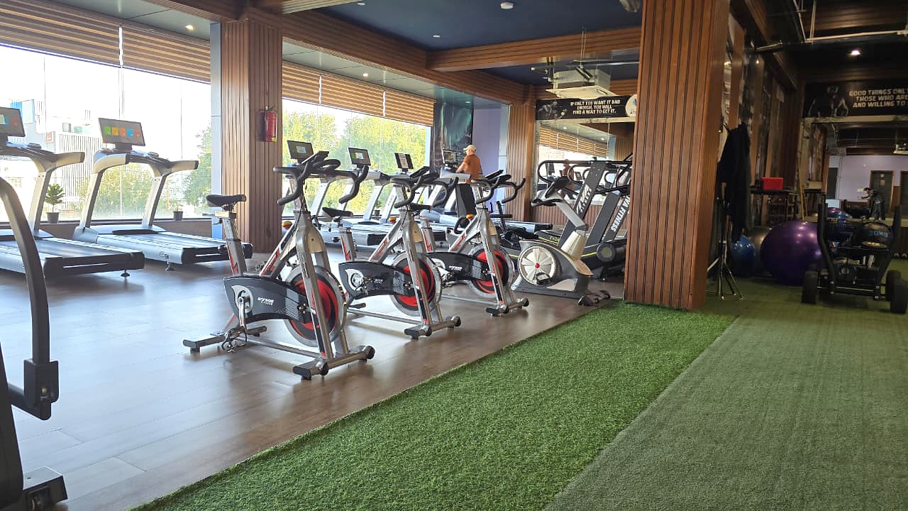 Stationary bikes and treadmills beside green turf and wood-paneled columns at V4 ATLANTIS.