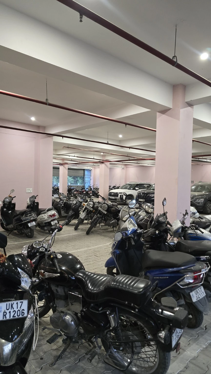 Cars and two-wheelers in the covered parking area beneath pale columns