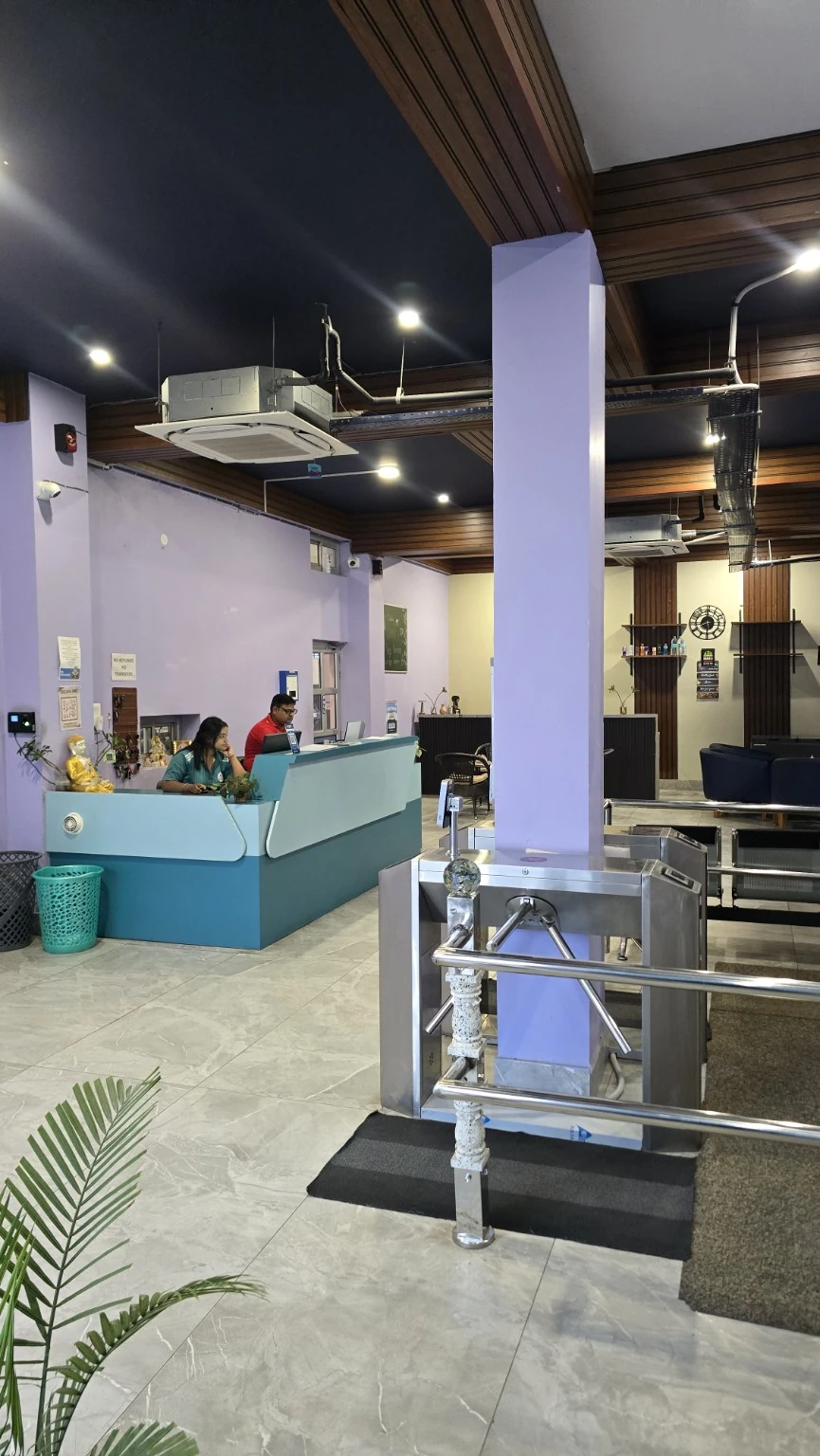 Turquoise reception desk beside an entrance gate with café seating in the background