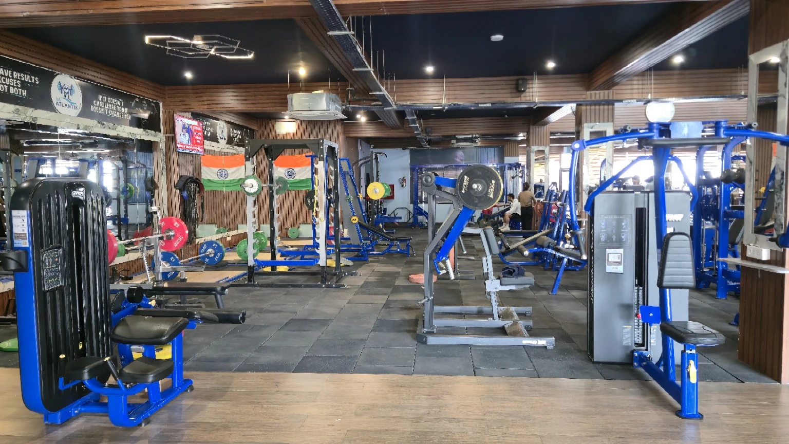 Wide strength floor with blue resistance machines, racks, coloured weight plates and mirrored timber walls