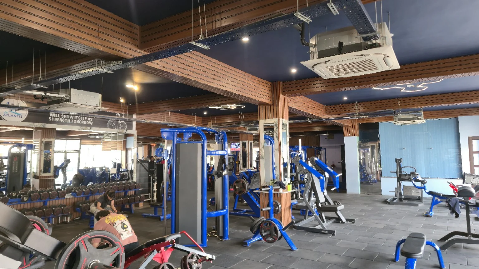 Wide strength floor with blue equipment, dumbbells, mirrors and timber columns