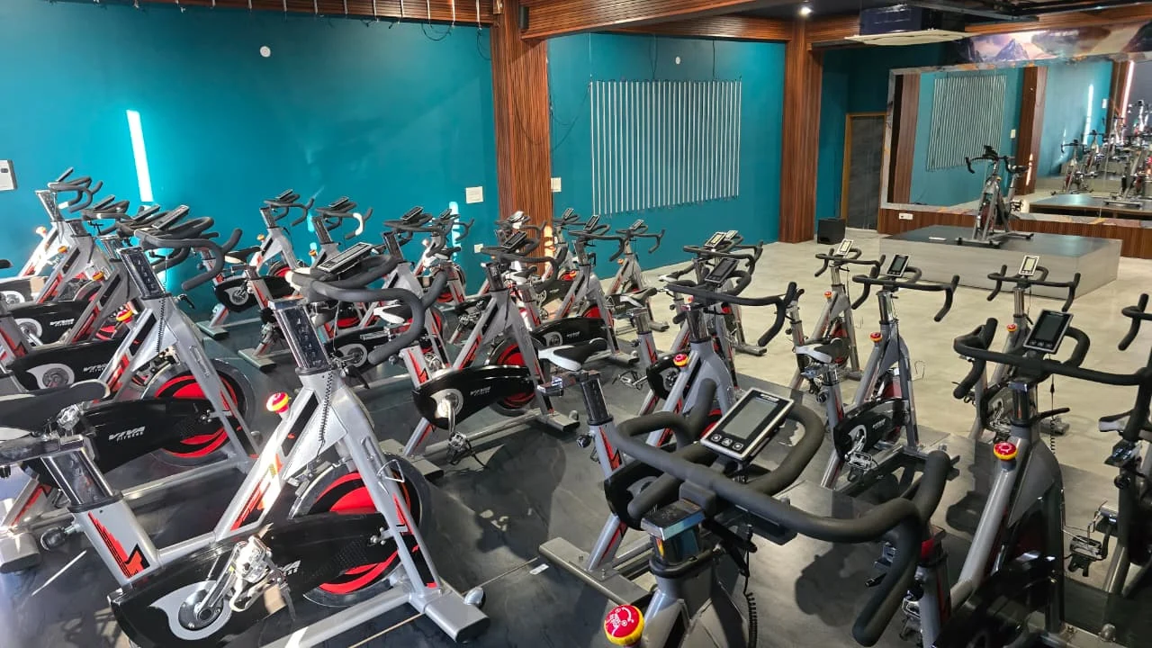 Close view of silver and red stationary spin bikes, with teal walls and a large wall mirror behind them.