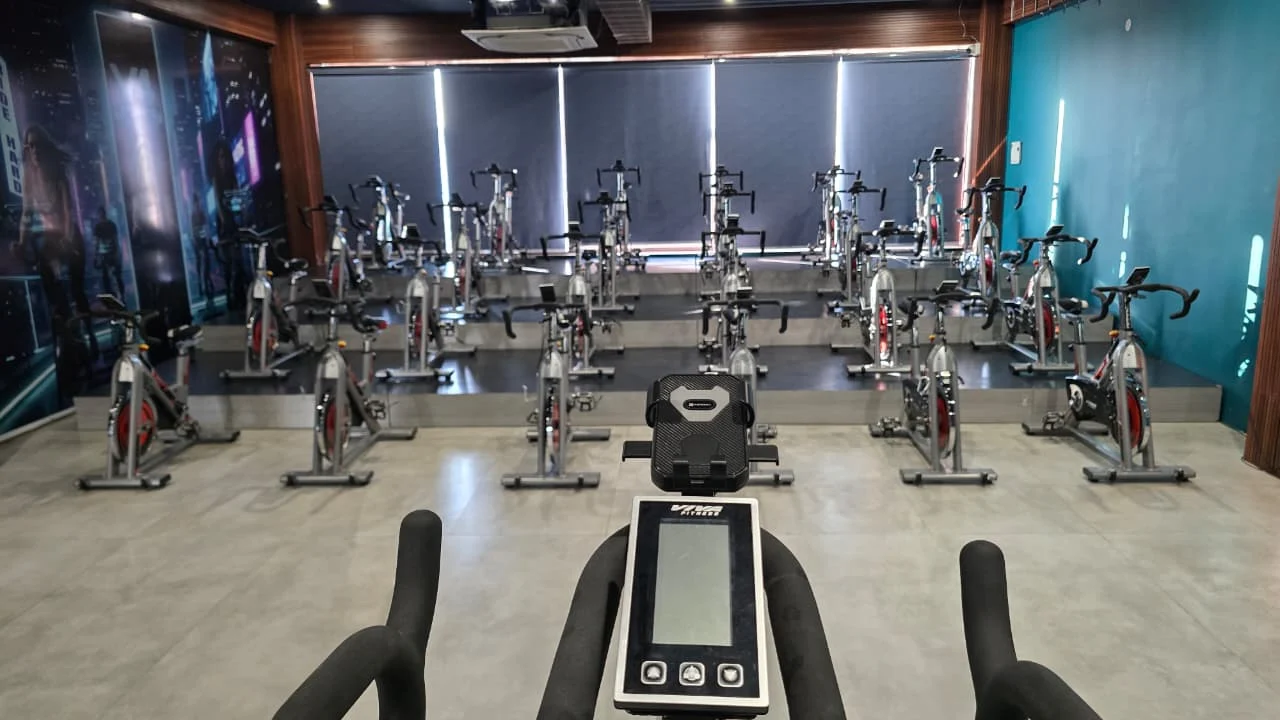 Rows of stationary spin bikes seen over a foreground bike’s console, facing the shaded windows of the spin studio.