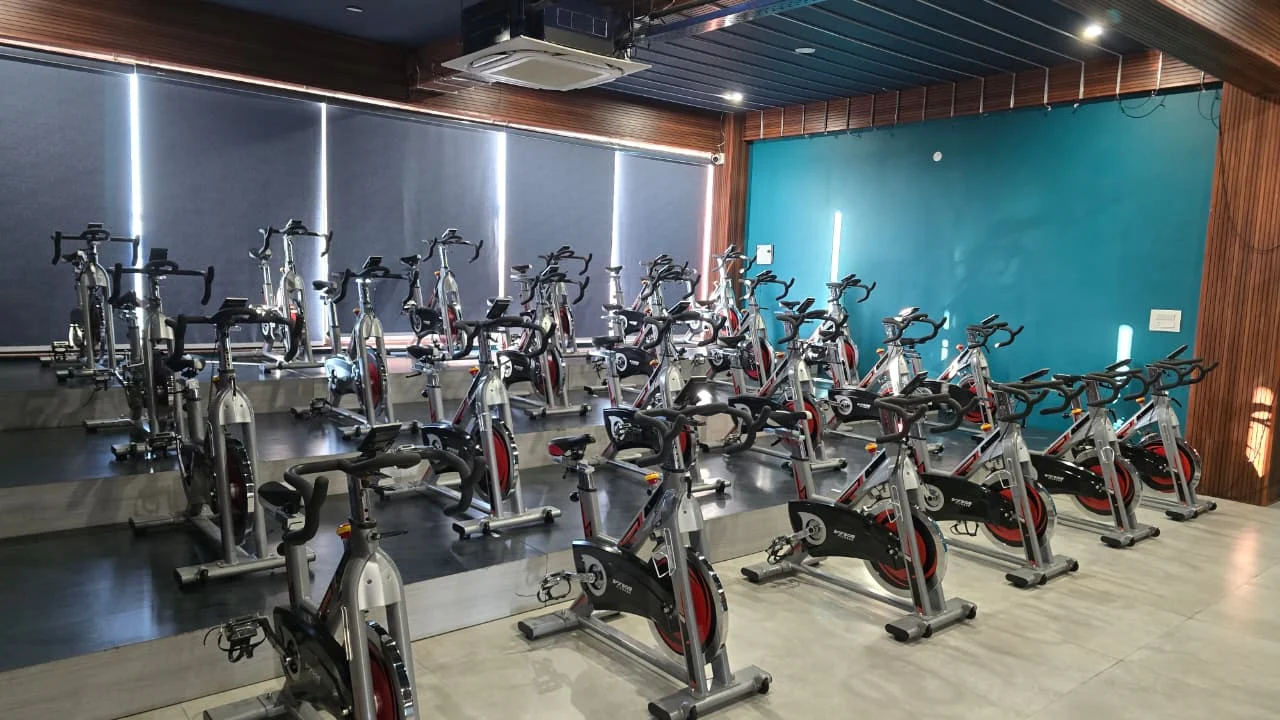 Rows of stationary spin bikes on stepped platforms beside shaded windows and a teal wall at V4 ATLANTIS.